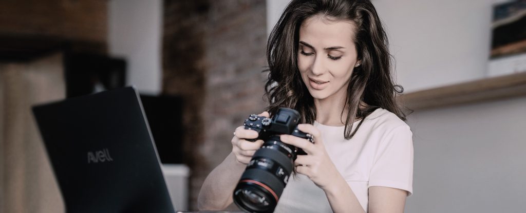 Fotógrafa analisando imagens em sua câmera ao lado de notebook Avell, ideal para edição de fotos profissionais.