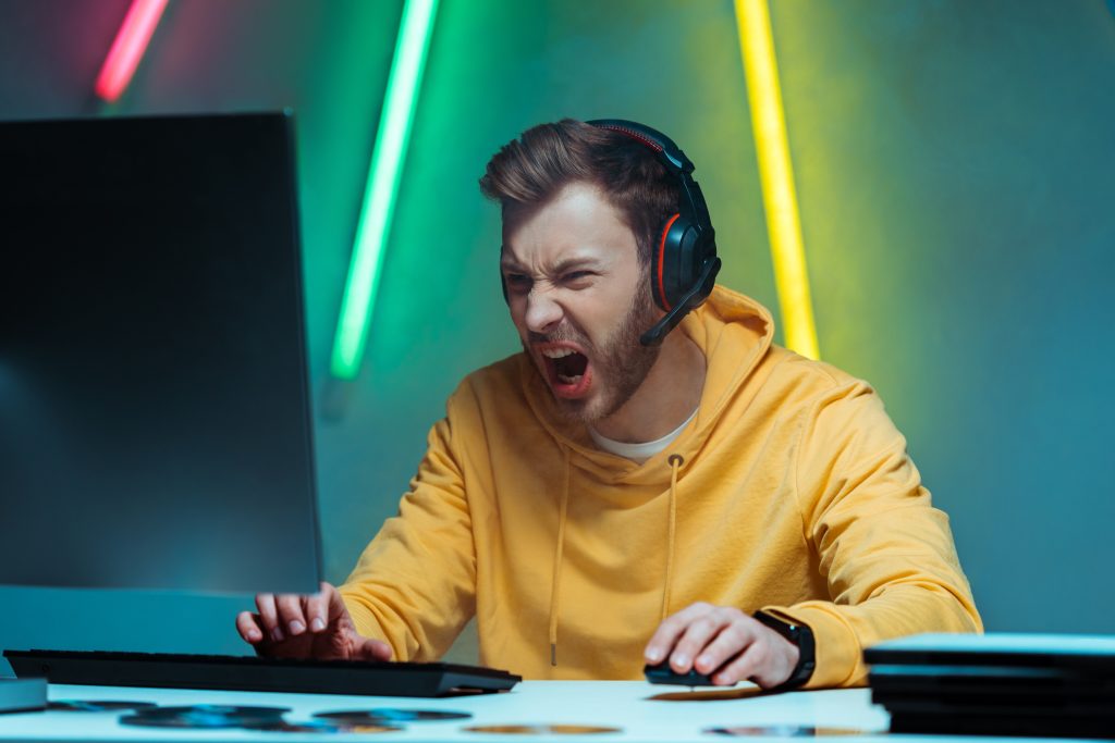 homem irritado e bonito em fones de ouvido jogando videogame com mouse e teclado de computador